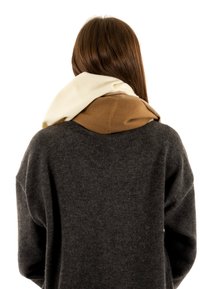 Meerkleurige sjaal in wit, beige en bruine tinten, met een zachte textuur en een gelaagd ontwerp, om de nek gewikkeld over een donkere trui.