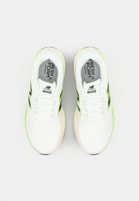 White athletic shoes with green accents, mesh upper, cushioned sole, and round toe. Features include logo and textured design elements.