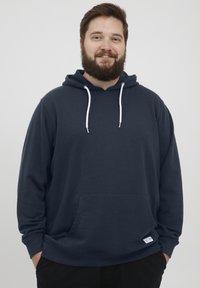 Sudadera azul marino, hecha de una mezcla de algodón, que presenta un bolsillo frontal, capucha con cordones ajustables y detalles blancos en el cuello y el dobladillo.