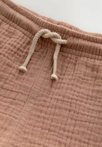 Pantalons de survêtement roses en textile avec une surface texturée, dotés d'une taille élastique et d'un cordon crémeux étroit avec des extrémités nouées.