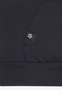Marineblauwe hoodie met geribbelde zoom, voorzien van een klein zwart label met een witte sterlogo. Zacht materiaal, detail van een kangoeroezak en een minimalistisch ontwerp.