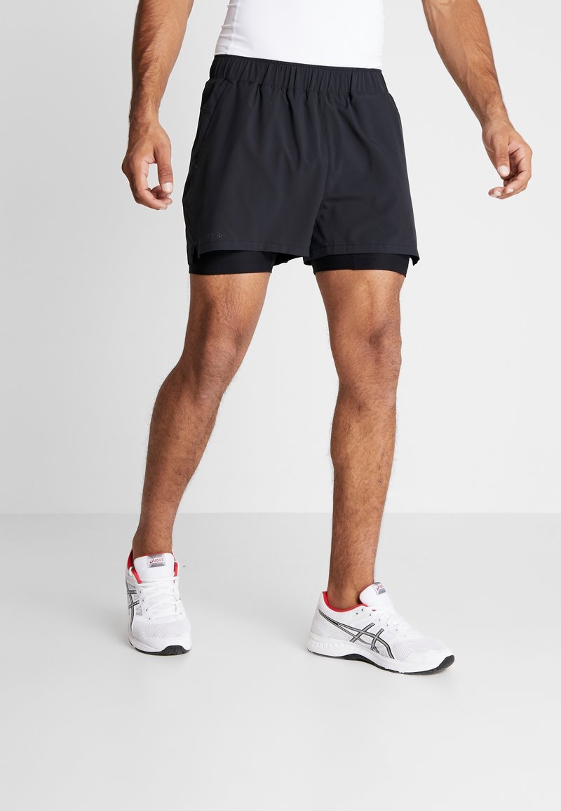 Shorts de sport noirs avec une ceinture élastique, présentant une coupe ample et une doublure intérieure, associés à des baskets blanches avec des accents rouges.