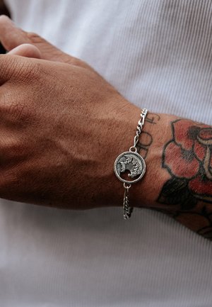 Silver chain bracelet featuring a circular pendant with a detailed design. Textured metal links and an intricate centerpiece enhance its appeal.