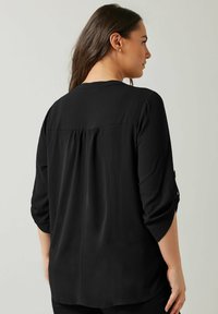 Sort bluse med en afslappet pasform, trekvartærmer og plisseret rygdetalje. Fremstillet af let, struktureret stof.