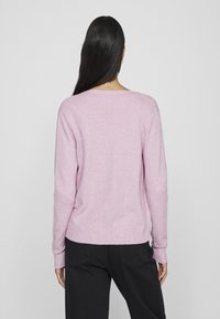 Helles pinker Pullover mit geripptem Saum und Bündchen, der einen lässigen Schnitt und einen weiten Ausschnitt aufweist. Kombiniert mit schwarzen Hosen, die ein schlichtes Design zeigen.