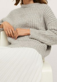 Harmaa neulottu pusero, jossa resorikuvio; pyöreä pääntie ja pitkät hihat. Päällä laskostetun valkoisen hameen p�äällä, esitellen kerroksellisen tyylin.