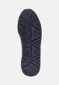 Must musta musta geomeetrilise mustriga ja süvistatud logoga "GUESS" esile tõstetud.