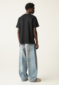 Schwarzes Baumwoll-T-Shirt mit rundem Ausschnitt, kombiniert mit hellblauen, weit geschnittenen Jeanshosen mit ausgewaschenem Look und Gesäßtaschen.