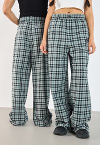 Gestreifte weite Hosen in Schwarz, Grün und Weiß. Elastischer Bund mit Knopf, entspannter Schnitt, weicher Stoff mit subtilen Musterdetails.