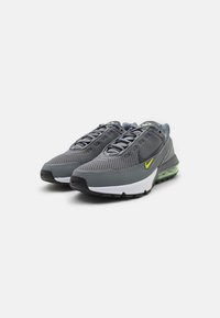 Zapatillas Nike con parte superior de malla en gris, acentuadas por un swoosh amarillo, una entresuela blanca en contraste y un amortiguador verde translúcido.