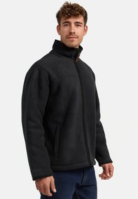 Chaqueta de forro polar negra con cuello alto, cierre de cremallera, dos bolsillos laterales y tejido texturizado. Diseño sencillo con costuras tonales y marca.