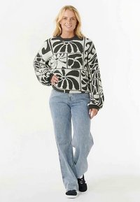 Jersey con estampado floral en blanco y negro, con cuello redondo y corte holgado, combinado con vaqueros azul claro y zapatillas negras.