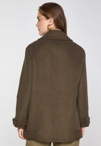 Cappotto di lana marrone con un design strutturato, colletto a punte e polsini con bottoni. Il tessuto appare morbido con una texture liscia.