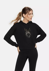 Black hoodie with long sleeves, a front pocket, and a gold outlined graphic of a heart and rabbit ears on the chest. Soft texture.