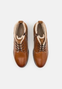 Botine din piele maro până la gleznă cu căptușeală din blană sintetică, având un design cu șireturi și închidere cu fermoar pe lateral pentru un acces ușor.