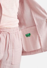 Chaqueta de lino rosa claro y pantalones a juego con una cinturilla elástica. La chaqueta cuenta con un bolsillo interior y las etiquetas son visibles.