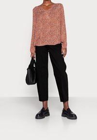 Blouse à manches longues et encolure en V de couleur rouge avec un imprimé floral blanc, associée à un pantalon noir droit. Portée avec des mocassins noirs à semelle épaisse et un sac à main.