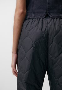 Černé prošívané kalhoty s texturovaným povrchem a elastickým pasem, v kombinaci s tmavým džínovým krátkým topem, který zdůrazňuje vrstvený design.