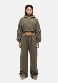 Olijf groene cropped hoodie met een voorrits en wit logo, gecombineerd met losse joggerbroeken met een elastische tailleband en logo.