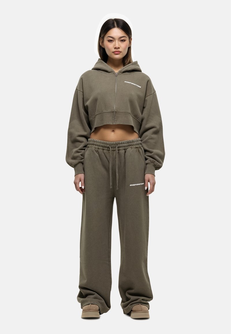 Olijf groene cropped hoodie met een voorrits en wit logo, gecombineerd met losse joggerbroeken met een elastische tailleband en logo.
