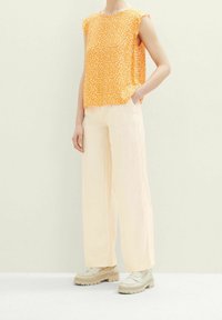 Pomarańczowa bluzka bez rękawów w kwiatowy wzór połączona z jasnobeżowymi spodniami typu wide-leg oraz masywnymi białymi sneakersami. Miękki, lekki materiał.