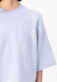 Lyseblå kortermet strikkegenser med rund halslinje, med myk tekstur og subtil glans, samt detaljer med raglan-søm.