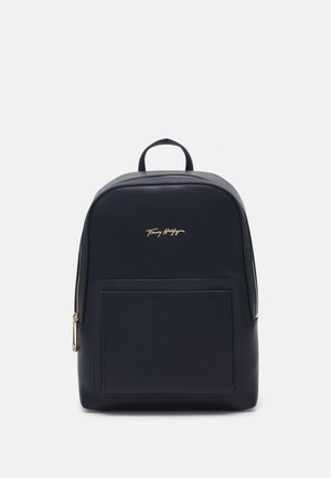 Zaino in pelle nera compatto con tasca frontale, zip dorata, maniglia superiore e piccolo logo dorato Tommy Hilfiger al centro anteriore.
