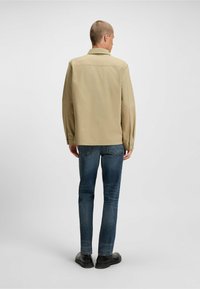 Beige lightweight jacket with a collar, straight cut, and long sleeves, paired with blue slim-fit jeans and black shoes.