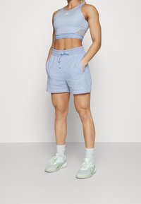 Ljusblå sportcrop-top med meshdetaljer, kombinerad med ljusblå shorts med elastisk midja och sidfickor. Vita sneakers med gröna accenter.