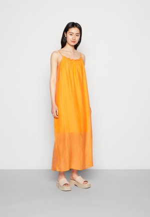 Vestido maxi laranja com alças finas, tecido texturizado e decote com franzidos. Combinado com sandálias de plataforma bege. Design simples e fluido.