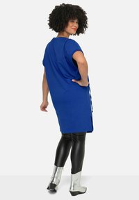 Blauwe tuniek met korte mouwen en zijsplitten, gedragen over zwarte leggings, gecombineerd met glanzende zilveren enkelboots. Glad oppervlak en een ontspannen pasvorm.