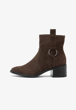 Braune Wildlederstiefeletten mit runder Spitze, seitlichem Reißverschluss und einer Schlaufe an der Rückseite für einfaches An- und Ausziehen. Mit einem klobigen schwarzen Absatz und minimalistischen Design.