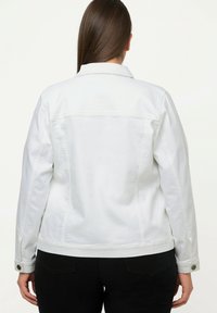 Bílá denimová bunda se strukturovaným designem, viditelným šitím a knoflíkovými detaily na manžetách, zobrazená ze zadní strany.