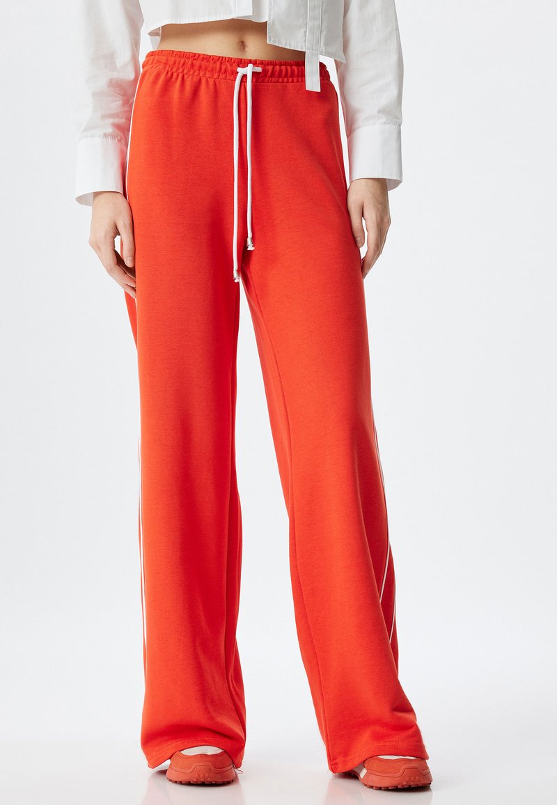 Rode joggingsbroek met een koord in de taille en witte accenten, gemaakt van zachte stof. Ze hebben een brede pijpdesign en reiken tot aan de schoenen.