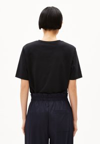 Zwarte T-shirt met korte mouwen en een ronde halslijn, gecombineerd met donkergekleurde broek met elastische taille en een achterzak. Soepele textuur.