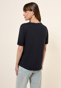 T-shirt à manches courtes bleu marine foncé avec un col rond et des manches roulées, fabriqué en matériau doux, associé à un jean bleu clair.