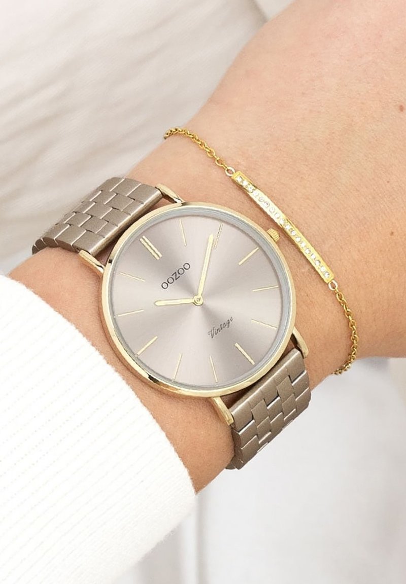 Montre en métal avec un cadran argenté rond et des aiguilles dorées, montée sur un bracelet tissé beige. Accompagnée d'un délicat bracelet en or.