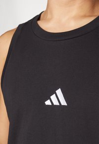 Camisola preta sem mangas feita de um tecido suave, com um logótipo Adidas branco e três riscas diagonais na frente.