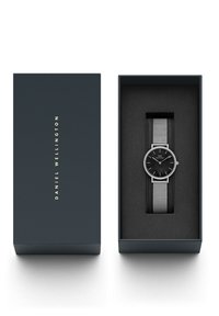 Must mustra mustra hõbevõrgust sang, musta dialiga, suletud tumedasse kasti. Kasti peal on brändi nimi "DANIEL WELLINGTON" kuldsete tähtedega.