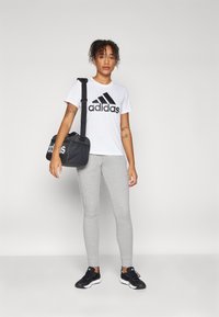 Hvit bomulls T-skjorte med svart "adidas" logo, grå leggins og svarte treningssko. Svart treningsbag med hvit logo. Frontvisning.