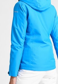 Helle blaue wasserdichte Jacke mit Kapuze, glatter Textur, tailliertem Design und verstellbaren Bündchen, mit einem Logo auf dem Oberarm.