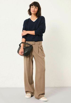 Navy knitted v-neck sweater, beige pleated wide-leg pants, black handbag with curved handle, and light-colored sneakers.