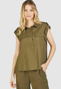 Olivgrüne Bluse mit kurzen Ärmeln, Knopfleiste, Taschen und lockerer Passform. Texturiertes Material, hinten leicht längerer Saum.