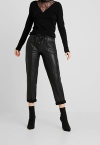 Pantaloni in pelle nera aderenti con vita regolabile e orli arrotolati, abbinati a una maglietta nera a maniche lunghe con scollatura in pizzo.