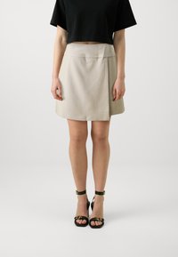 Beige skjørt med rett snitt og teksturert stoff. Kombinert med svarte høyhælte sandaler med gullhardware.