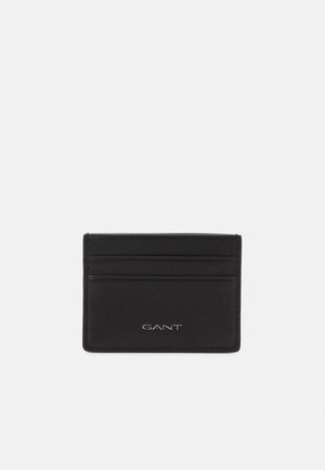 Porte-cartes en cuir noir avec quatre fentes pour cartes, texture lisse et logo GANT embossé à l'avant. Design rectangulaire simple.