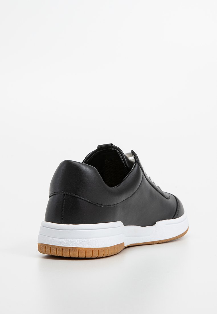 Zapatilla de cuero negro con suela de goma blanca y detalles en goma. Presenta un diseño elegante y forma redondeada con un collar acolchado.