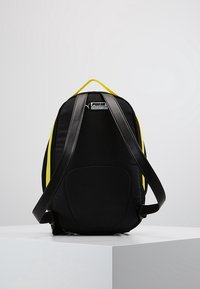 Mochila negra con acentos amarillos contrastantes, que cuenta con un respaldo acolchado, correas ajustables y un logo distintivo en la parte superior.
