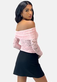 Rosa blonde off-shoulder top med lange blonde ærmer, parret med en fitted sort mini-nederdel. Glatte teksturer og detaljeret blonde mønster.