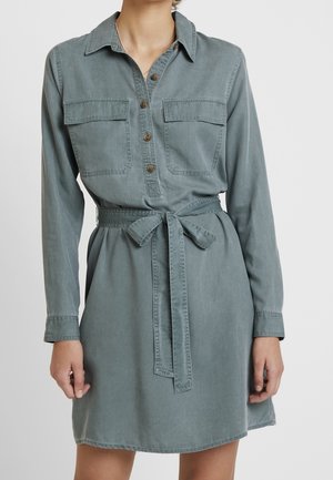 Jasnoszara sukienka dżinsowa z długimi rękawami, zapięciem na guziki z przodu, dwoma kieszeniami na piersiach, paskiem w talii i luźnym krojem.